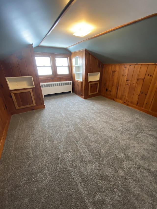 bonus room with lofted ceiling, dark colored carpet, wood walls, and radiator