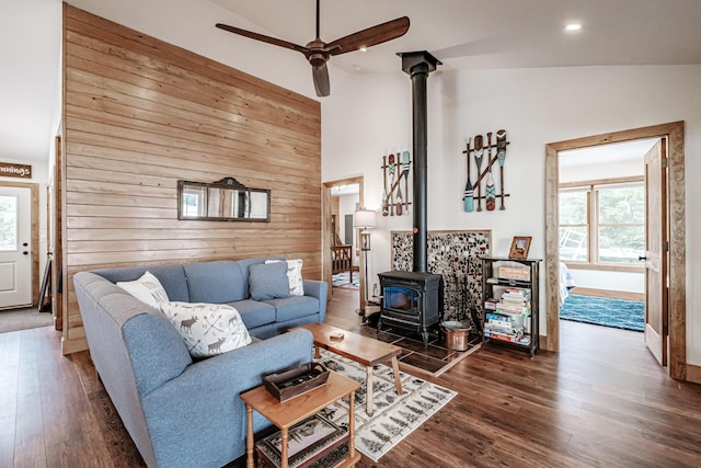 living room with dark hardwood / wood-style flooring, wooden walls, a wood stove, high vaulted ceiling, and ceiling fan