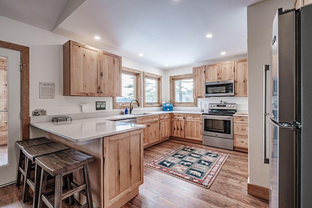 kitchen with kitchen peninsula, light brown cabinetry, appliances with stainless steel finishes, and a kitchen bar