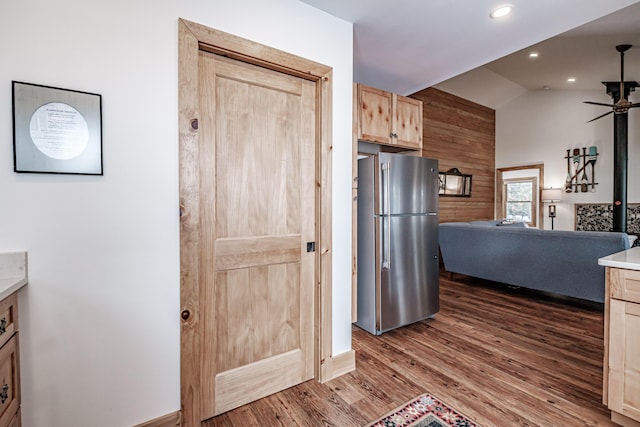 kitchen with ceiling fan, vaulted ceiling, stainless steel refrigerator, wooden walls, and light brown cabinetry