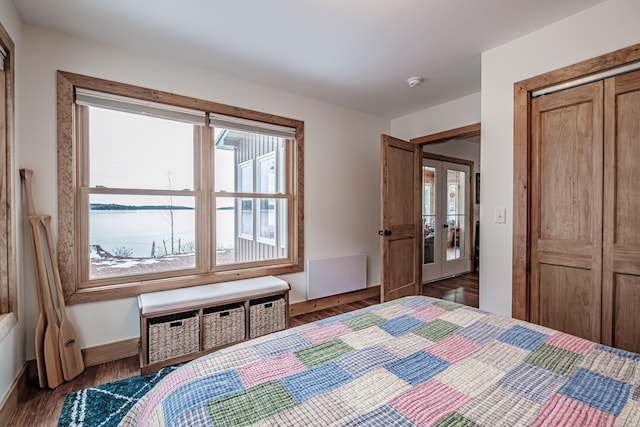 bedroom with dark hardwood / wood-style floors, a closet, a water view, and french doors