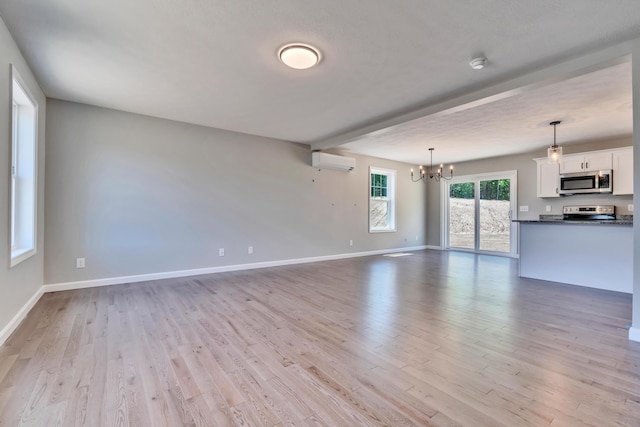 unfurnished living room featuring an AC wall unit, light wood-type flooring, and an inviting chandelier