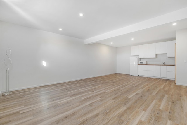 unfurnished living room with beam ceiling and light hardwood / wood-style floors