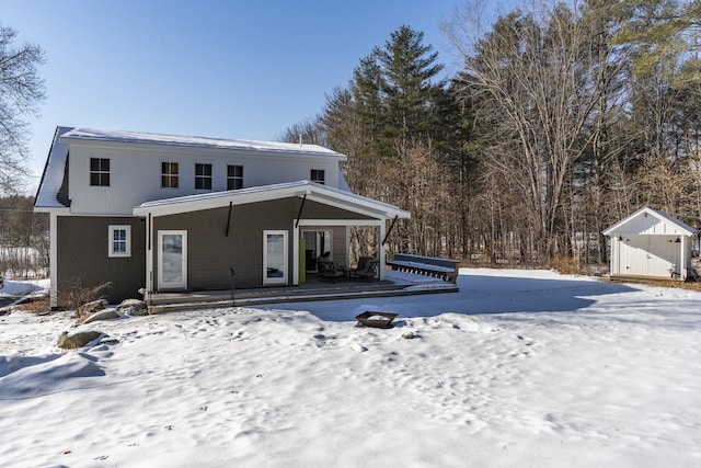 snow covered rear of property featuring a shed