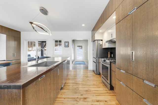 kitchen featuring appliances with stainless steel finishes, pendant lighting, sink, a center island, and light wood-type flooring