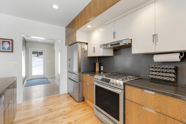 kitchen with white cabinetry, light wood-type flooring, appliances with stainless steel finishes, dark stone counters, and backsplash