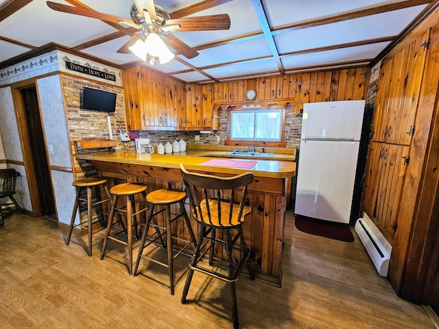 kitchen with a kitchen bar, kitchen peninsula, a baseboard heating unit, white refrigerator, and sink