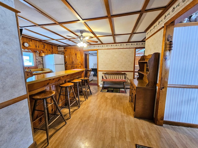 kitchen featuring white fridge, light wood-type flooring, ceiling fan, a breakfast bar, and coffered ceiling