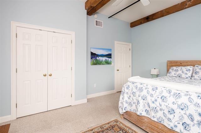 carpeted bedroom with ceiling fan, a closet, and beamed ceiling