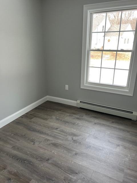 empty room featuring a baseboard heating unit and dark hardwood / wood-style flooring