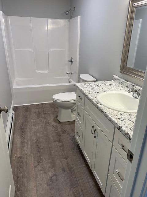 full bathroom with toilet, bathing tub / shower combination, a baseboard heating unit, wood-type flooring, and vanity