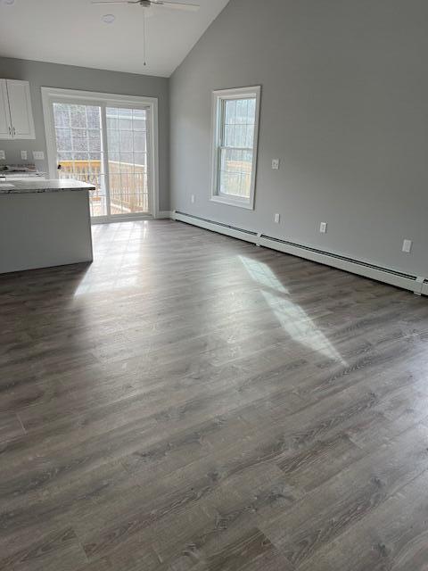 unfurnished living room featuring ceiling fan, dark wood-type flooring, a baseboard radiator, and vaulted ceiling