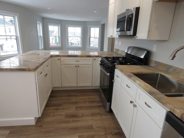 kitchen with a sink, light countertops, a peninsula, appliances with stainless steel finishes, and dark wood-style floors