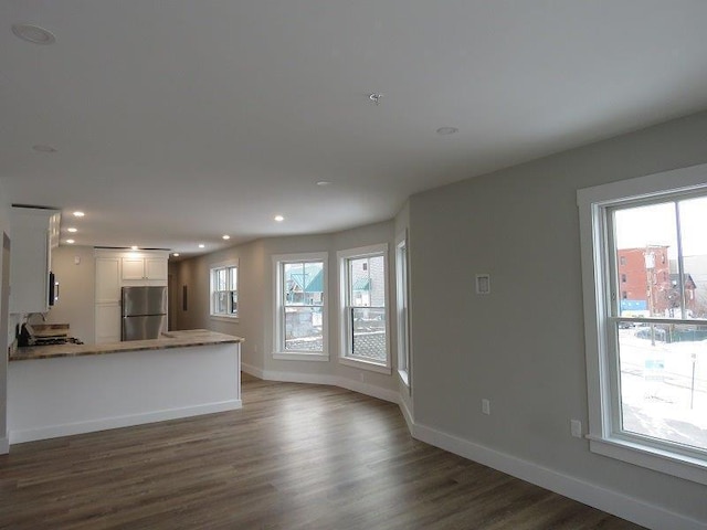 unfurnished living room featuring dark wood finished floors, plenty of natural light, and baseboards