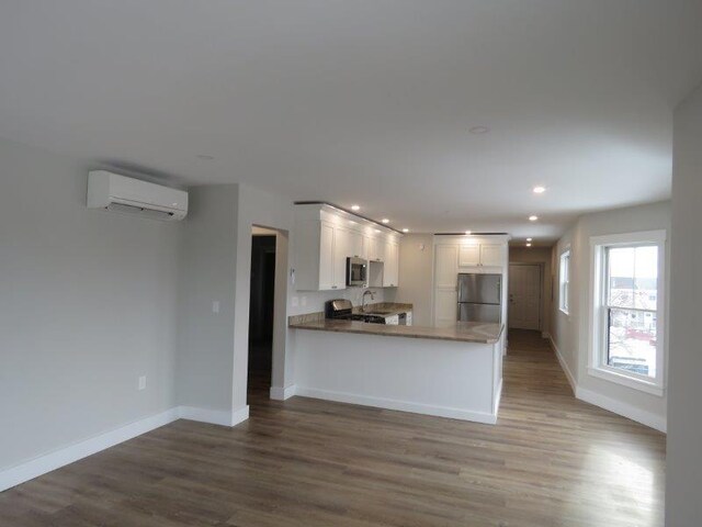 kitchen with white cabinets, a peninsula, an AC wall unit, wood finished floors, and appliances with stainless steel finishes