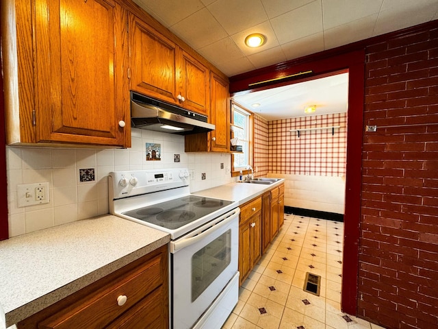 kitchen featuring sink, backsplash, brick wall, a drop ceiling, and white electric stove