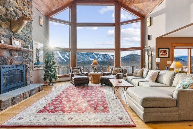 living room with a healthy amount of sunlight, a mountain view, a stone fireplace, and high vaulted ceiling