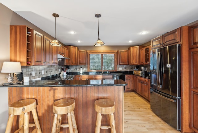 kitchen featuring black appliances, a kitchen bar, decorative light fixtures, decorative backsplash, and kitchen peninsula