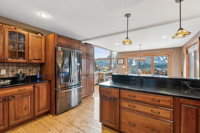 kitchen featuring pendant lighting, dark stone counters, tasteful backsplash, light wood-type flooring, and fridge with ice dispenser