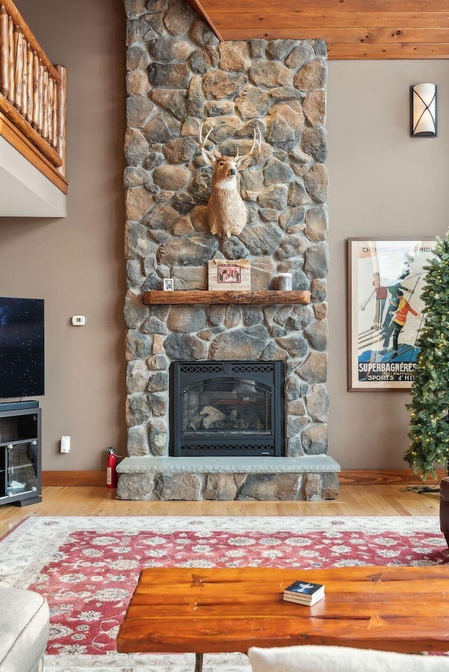 living room with wood-type flooring, a stone fireplace, and wooden ceiling