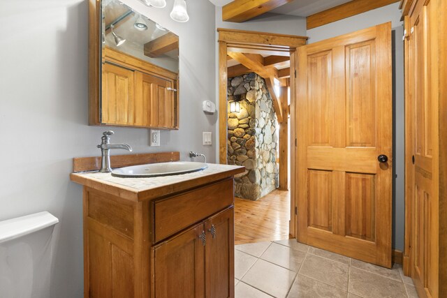 bathroom with toilet, vanity, beam ceiling, and tile patterned flooring