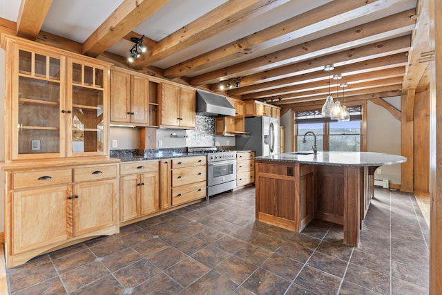 kitchen featuring appliances with stainless steel finishes, wall chimney range hood, beamed ceiling, sink, and a kitchen island with sink