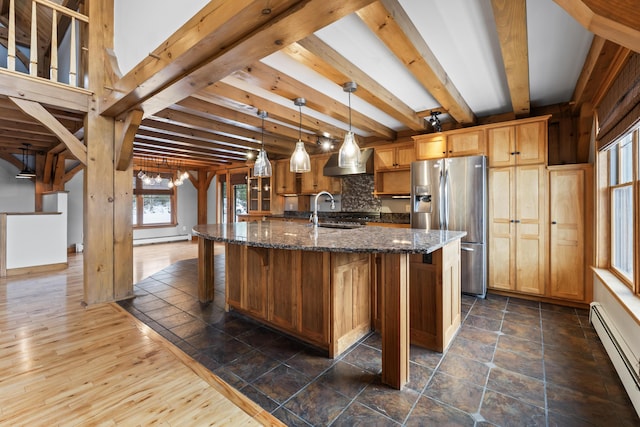 kitchen featuring pendant lighting, stainless steel refrigerator with ice dispenser, a kitchen island with sink, dark stone counters, and a baseboard radiator