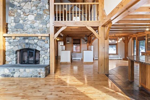 unfurnished living room with hardwood / wood-style floors, a baseboard heating unit, and a stone fireplace