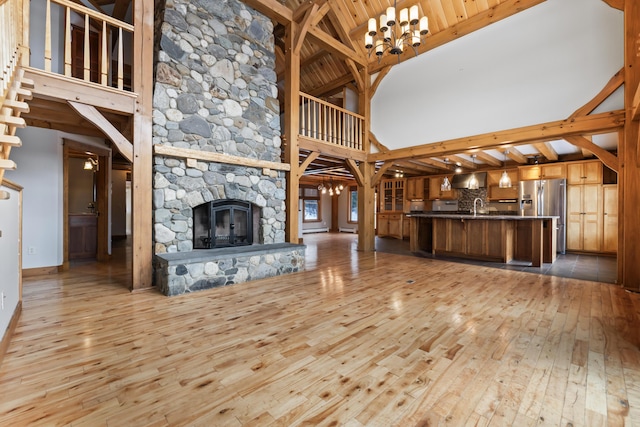 unfurnished living room featuring high vaulted ceiling, sink, a stone fireplace, and light wood-type flooring