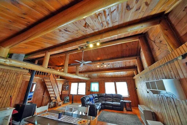 living room with rail lighting, ceiling fan, hardwood / wood-style floors, lofted ceiling with beams, and a wood stove