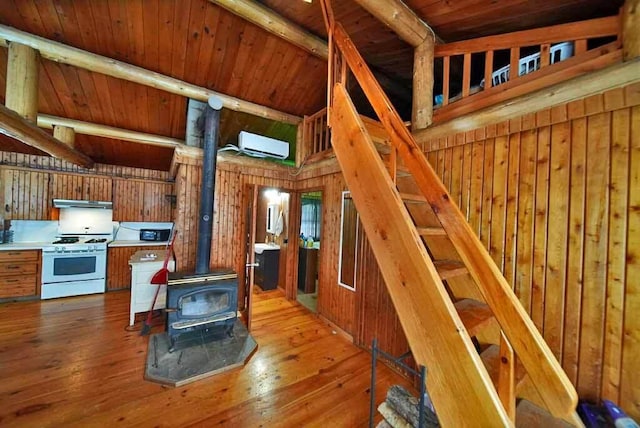 kitchen with white gas stove, wood walls, a wood stove, a wall unit AC, and light hardwood / wood-style floors