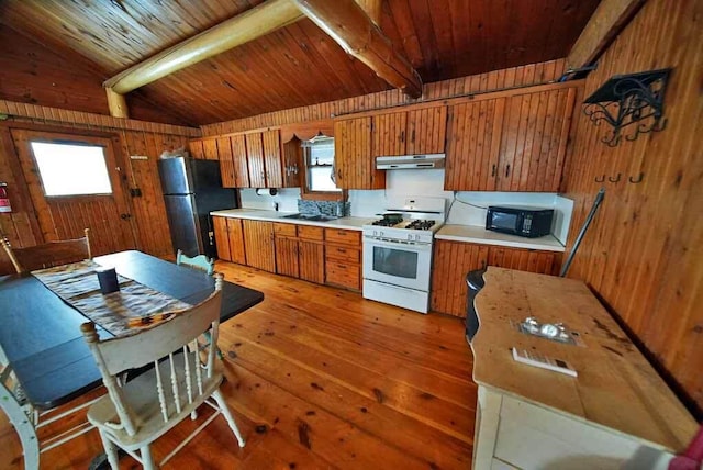 kitchen featuring gas range gas stove, stainless steel refrigerator, vaulted ceiling with beams, wooden walls, and dark hardwood / wood-style flooring