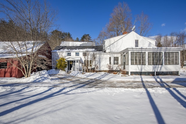 snow covered back of property featuring a sunroom