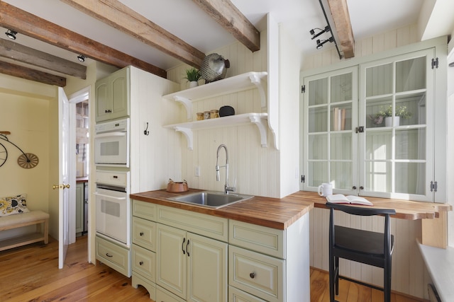 kitchen with sink, beam ceiling, wooden counters, and light wood-type flooring