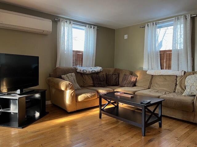 living room with an AC wall unit, plenty of natural light, and light hardwood / wood-style flooring