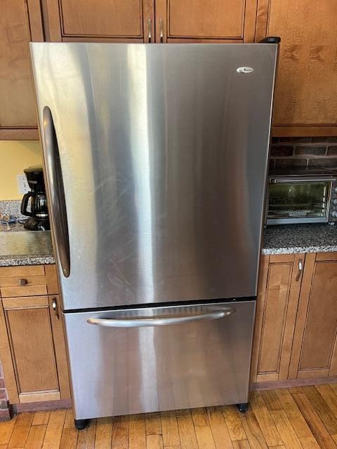 interior details featuring stainless steel refrigerator, light hardwood / wood-style flooring, and dark stone countertops