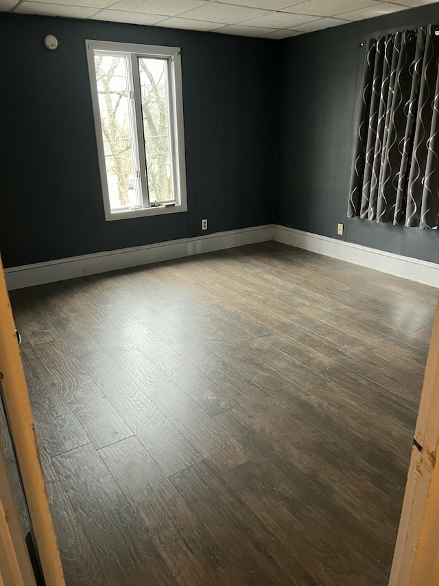 unfurnished room featuring wood finished floors, a paneled ceiling, and baseboards