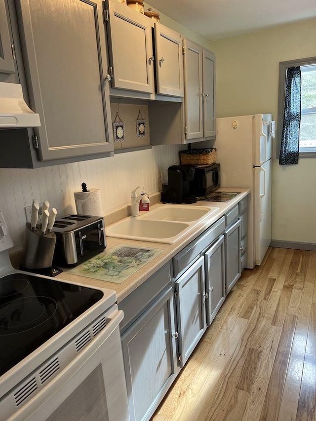 kitchen featuring light wood-type flooring, white appliances, sink, and gray cabinetry