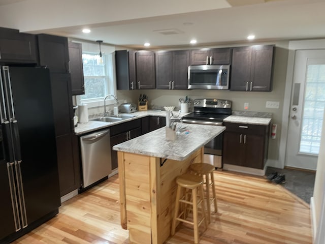 kitchen with a center island, stainless steel appliances, sink, light hardwood / wood-style flooring, and dark brown cabinets