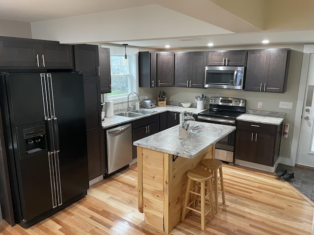 kitchen featuring appliances with stainless steel finishes, a kitchen island, a kitchen bar, light hardwood / wood-style floors, and sink