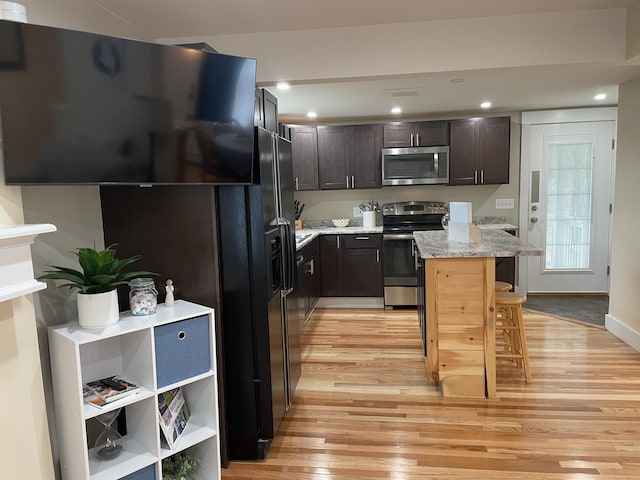 kitchen with stainless steel appliances, light stone countertops, light hardwood / wood-style floors, a breakfast bar area, and dark brown cabinetry