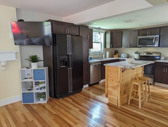 kitchen featuring appliances with stainless steel finishes, a kitchen breakfast bar, sink, dark brown cabinetry, and light hardwood / wood-style flooring