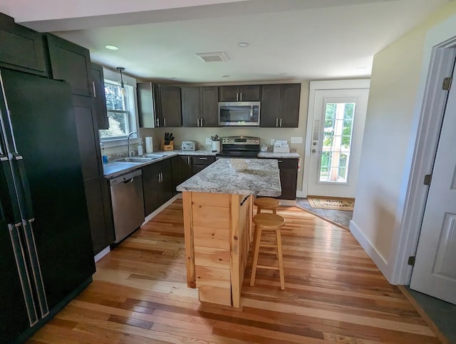 kitchen featuring appliances with stainless steel finishes, a center island, sink, light stone counters, and light hardwood / wood-style flooring