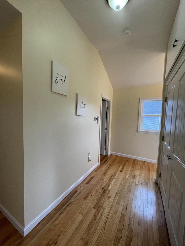 corridor featuring light wood-type flooring and vaulted ceiling