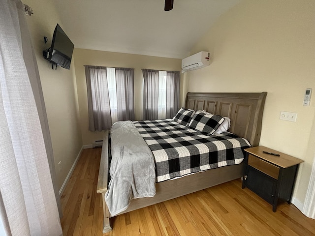 bedroom with lofted ceiling, light hardwood / wood-style floors, an AC wall unit, and ceiling fan