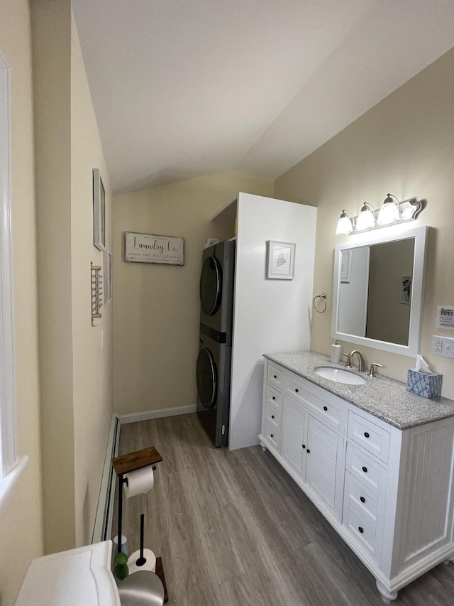 bathroom featuring vanity, hardwood / wood-style floors, stacked washer / dryer, and lofted ceiling