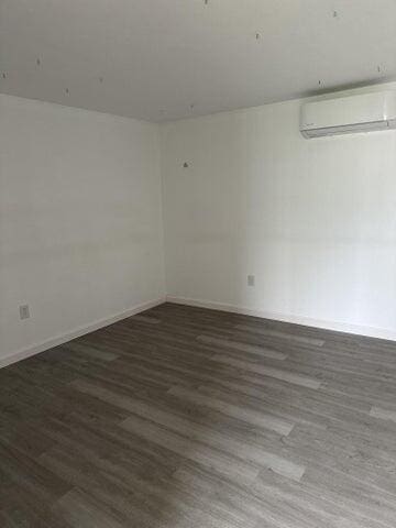 unfurnished room featuring dark wood-type flooring and a wall mounted AC