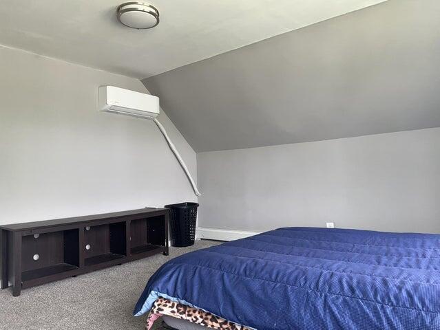 carpeted bedroom featuring lofted ceiling and a wall mounted AC