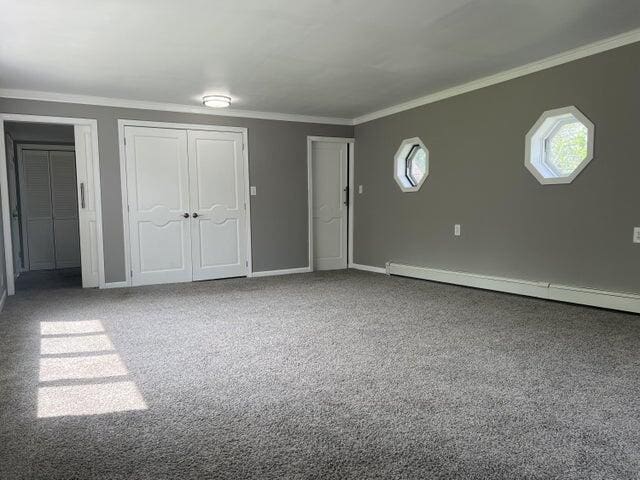 interior space with a baseboard heating unit, ornamental molding, and carpet floors