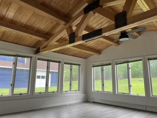 unfurnished sunroom featuring ceiling fan, lofted ceiling with beams, a baseboard heating unit, and wooden ceiling